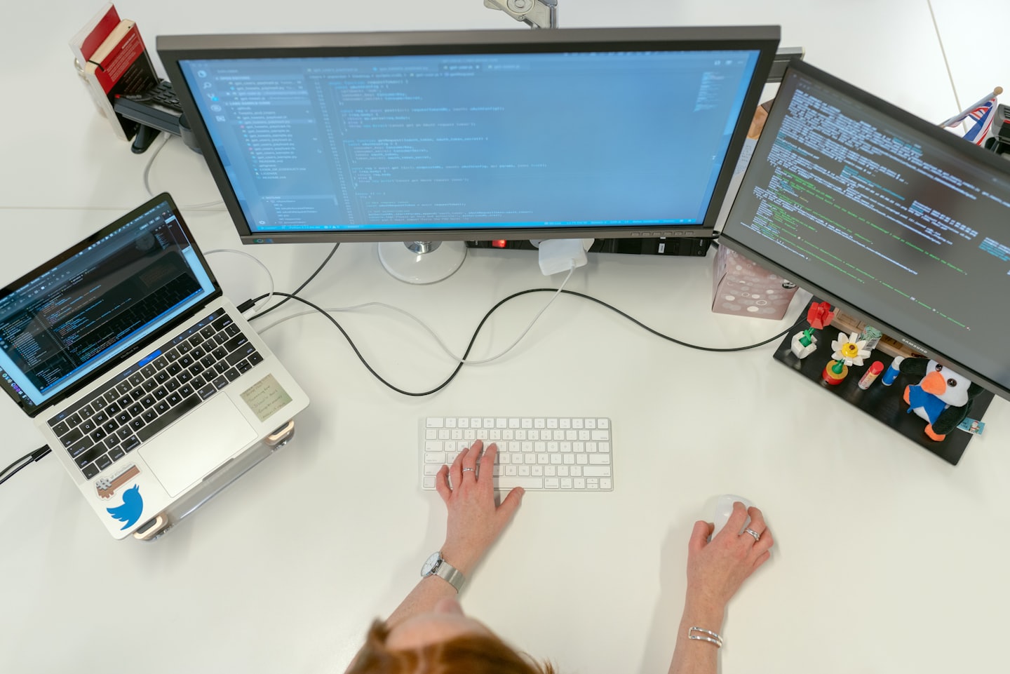 Programador escribiendo código en un puesto de trabajo con varios monitores en una oficina.