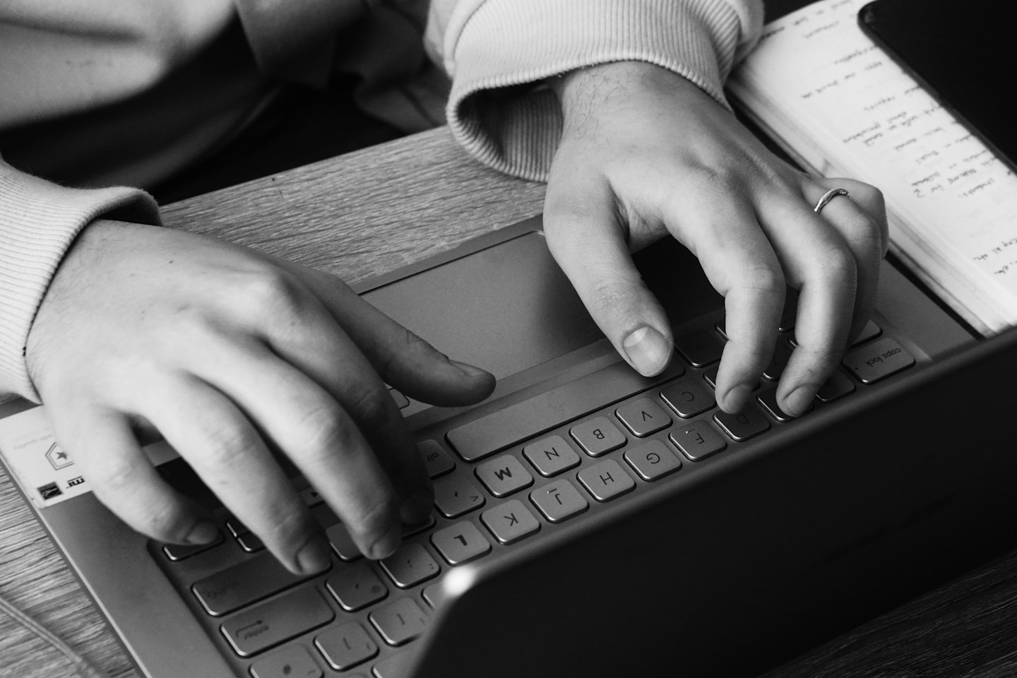 Manos escribiendo en un teclado de portátil plateado sobre un escritorio de madera.